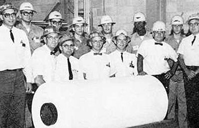 About a dozen men in hardhats stand around a newly-made giant roll of Tyvek.