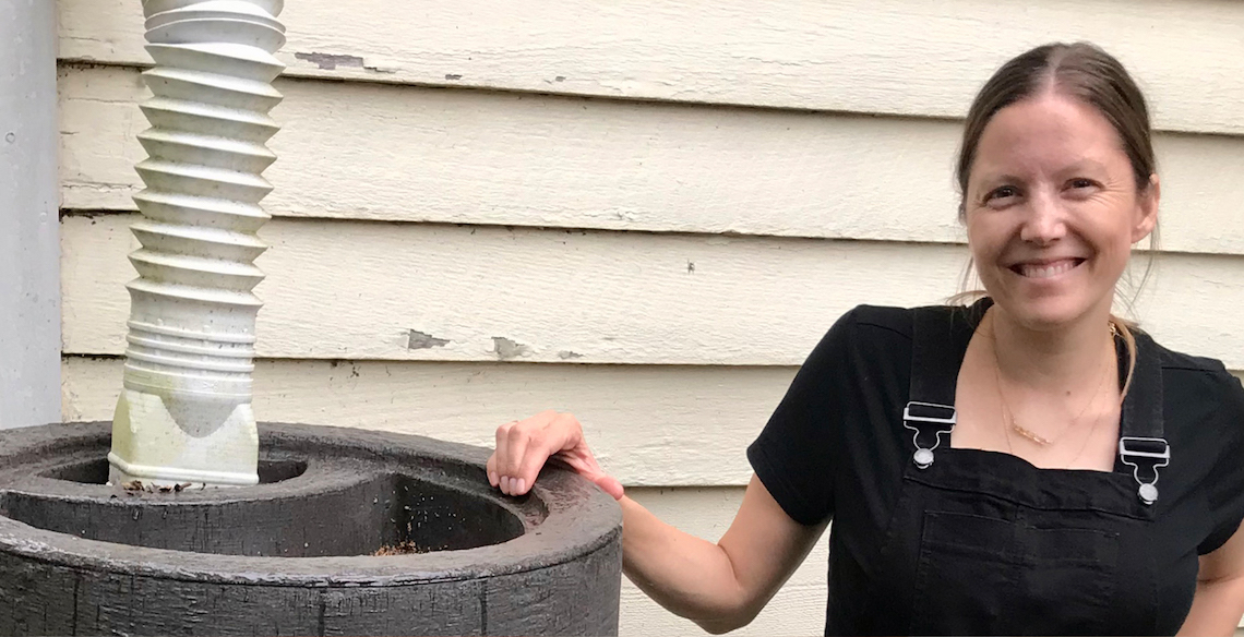 Amanda Rockler with right hand on rain barrell.