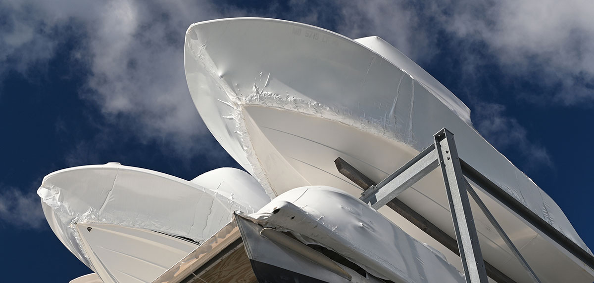 Photo of three 25 foot boats wrapped in white shrink wrap. Image taken from the ground. The boats are on the top level of an outdoor dry dock facility, or boatel. Photo, Lisa D. Tossey / MDSG