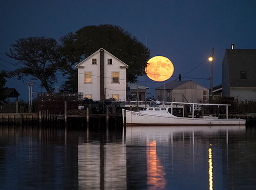 A blood moon rises over a waterman’s home and workboat on Smith Island. Photograph courtesy of David Harp
